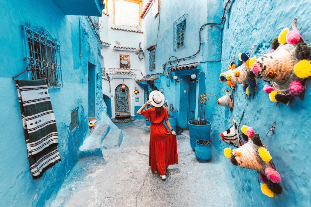 Young woman with red dress visiting the blue city Chefchaouen, Morocco