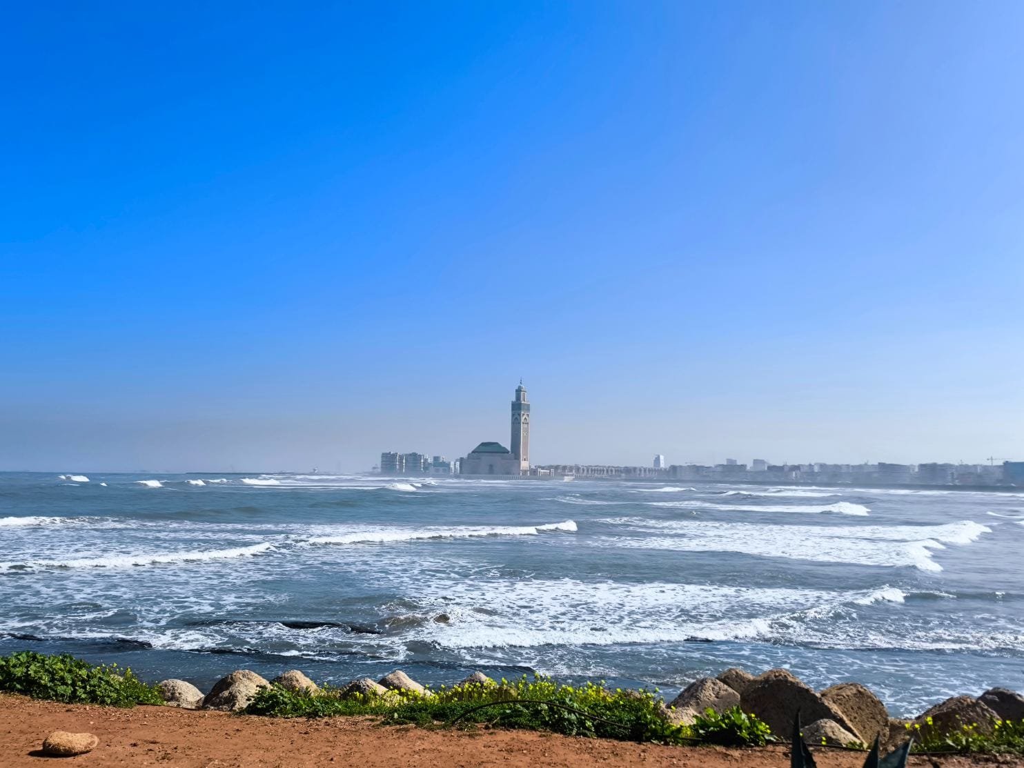 Majestic view of the Hassan II Mosque in Casablanca, Morocco, rising dramatically above the Atlantic Ocean waters, with its towering minaret, ornate Moorish façade, and vast marble esplanade reflecting the golden light over the sea.