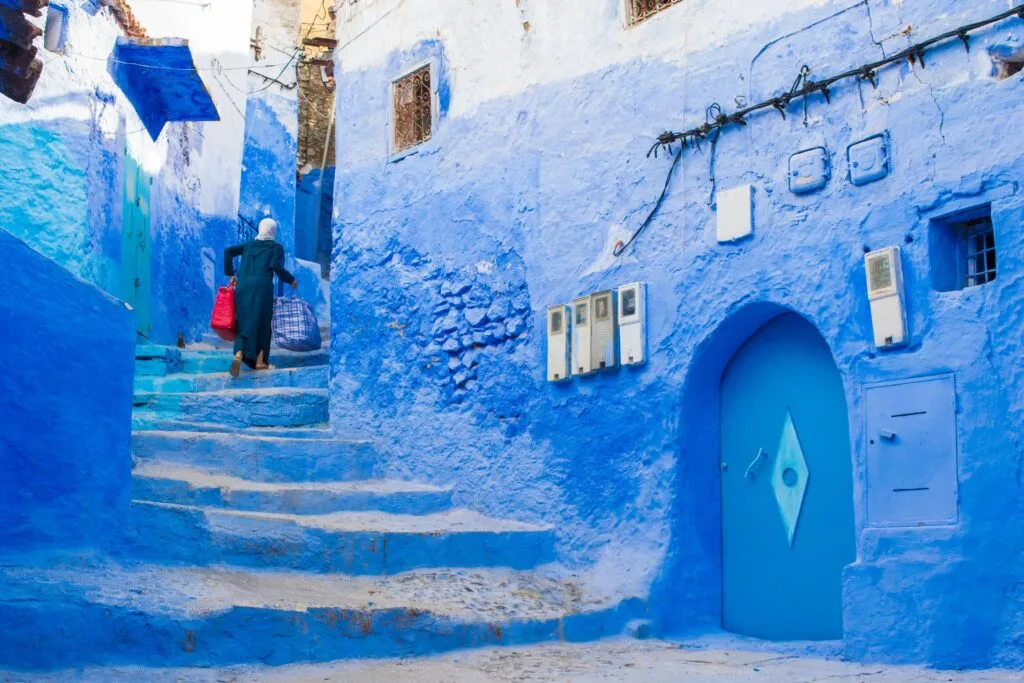 Blue-painted street in Chefchaouen, Morocco, with traditional doors, stairs, and medina charm.