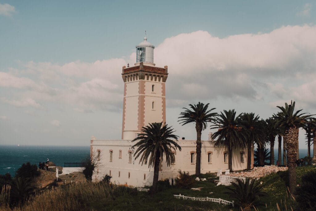 Beautiful aged lighthouse near tropical trees, sea and cloudy sky in Chefchaouen, Morocco