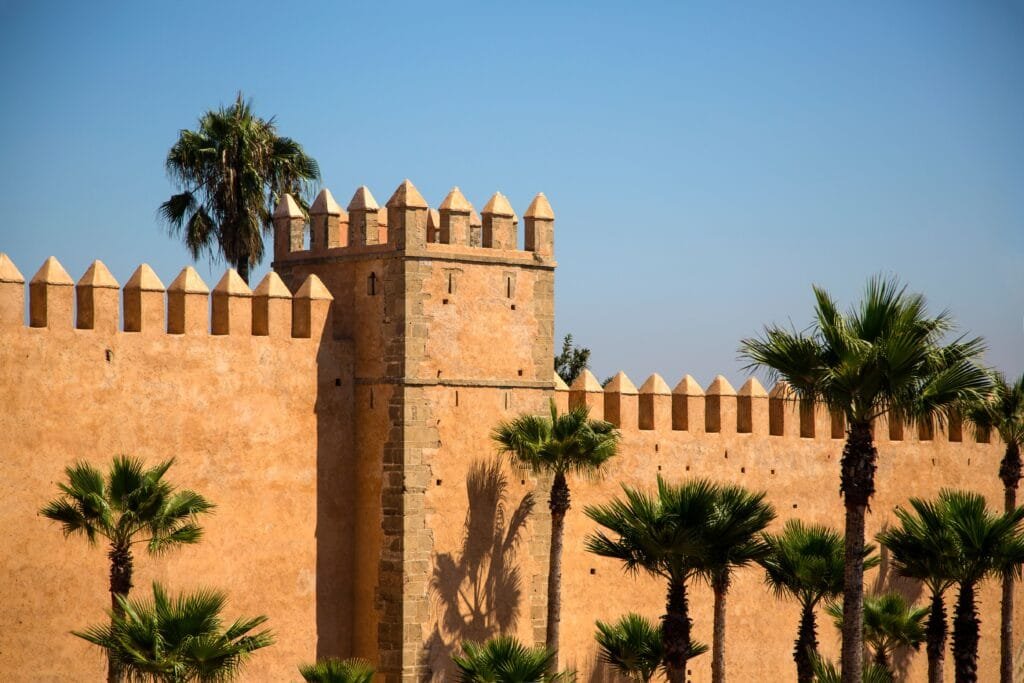 A section of the ancient Almohad-era stone fortification wall in Rabat, Morocco, featuring traditional ochre-colored masonry with crenellated battlements, set against a clear sky.