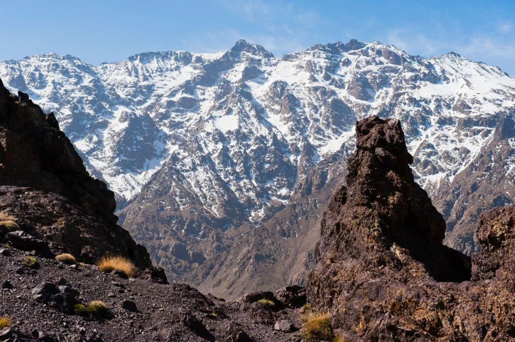 Dramatic High Atlas Mountain scenery along the trekking route between Ouirgane and Imlil in Morocco, with rugged snow-dusted peaks, deep valleys, terraced hillsides and traditional Berber villages dotting the breathtaking landscape.